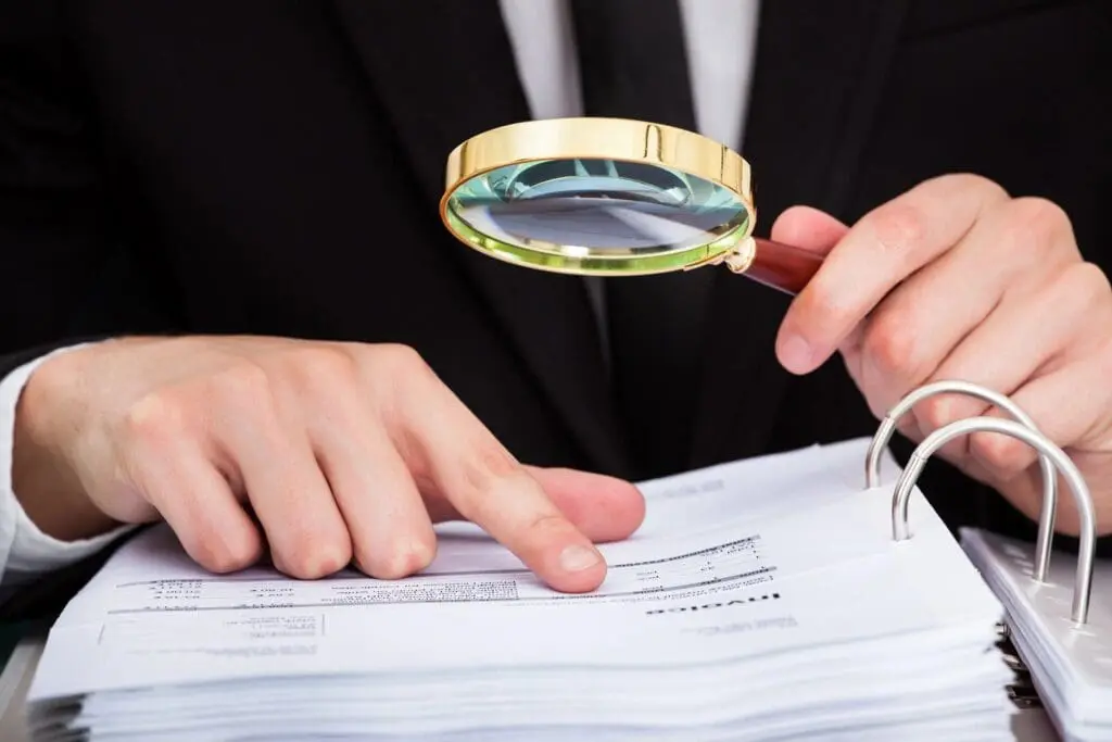 Person examining documents with a magnifying glass.